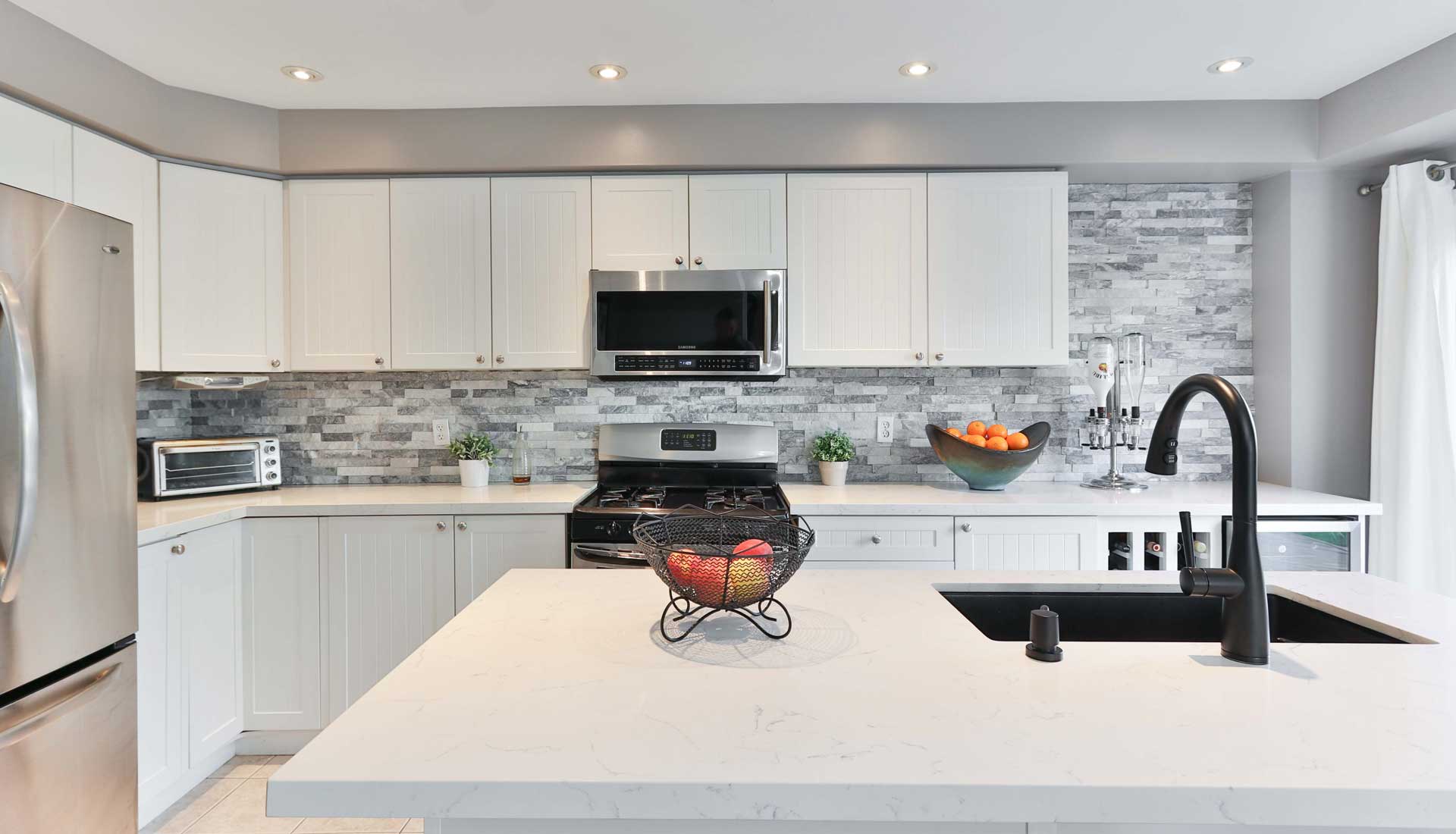 White kitchen island with black sink and faucet sits in front of a white kitchen countertop with white cabinetry and a black stove