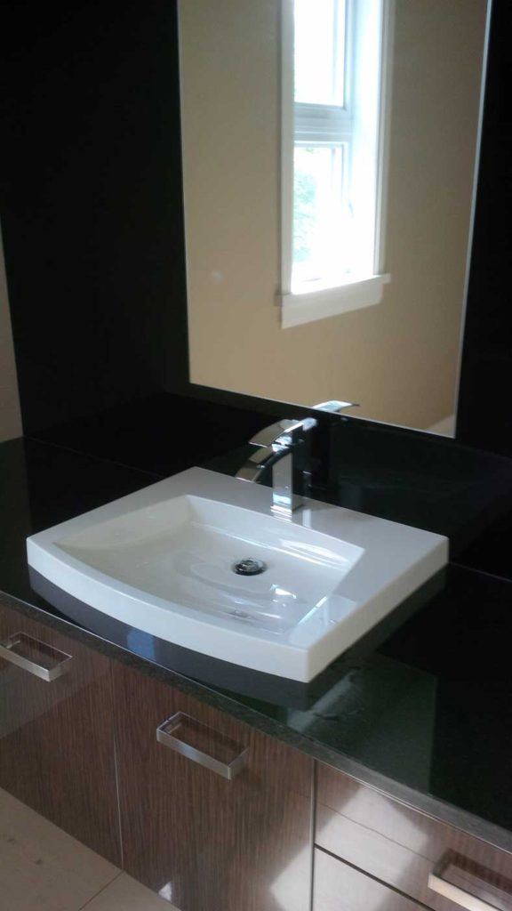 White bathroom sink sits on black countertop with mirror above