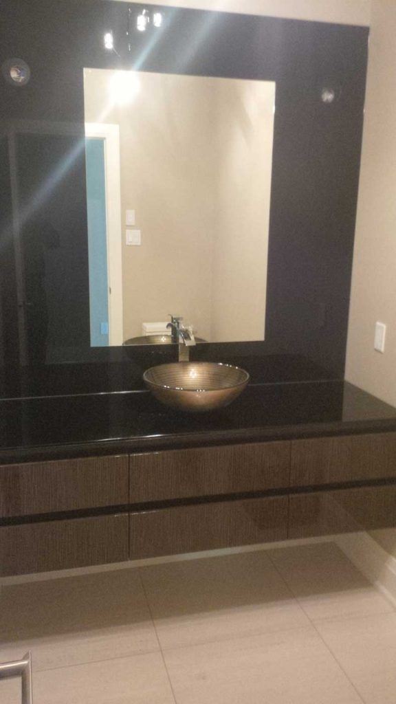 Bathroom sink bowl on brown countertop with brown-framed mirror above