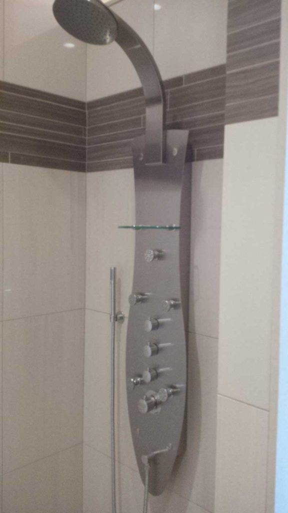 Metal shower faucet set in a stand-up shower with brown & beige tiles.