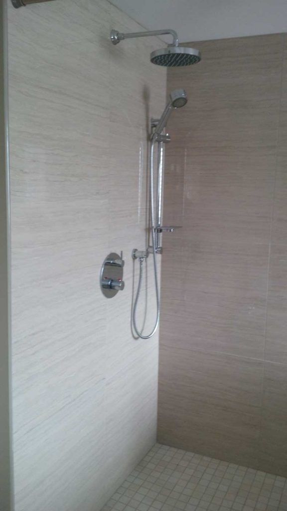 Shower faucet in a stand-up shower with beige walls and beige floor tiles