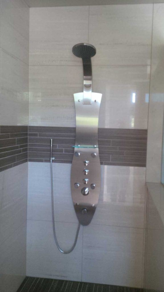 Metal shower faucet set in a stand-up shower with brown & biege tiles.