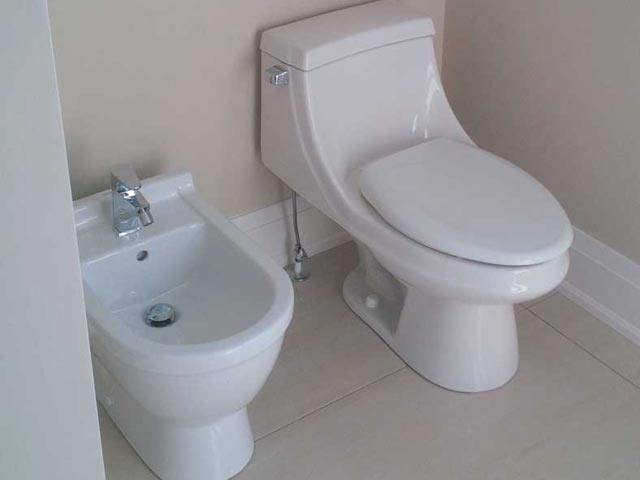 White bidet to the left of a white toilet in a white bathroom
