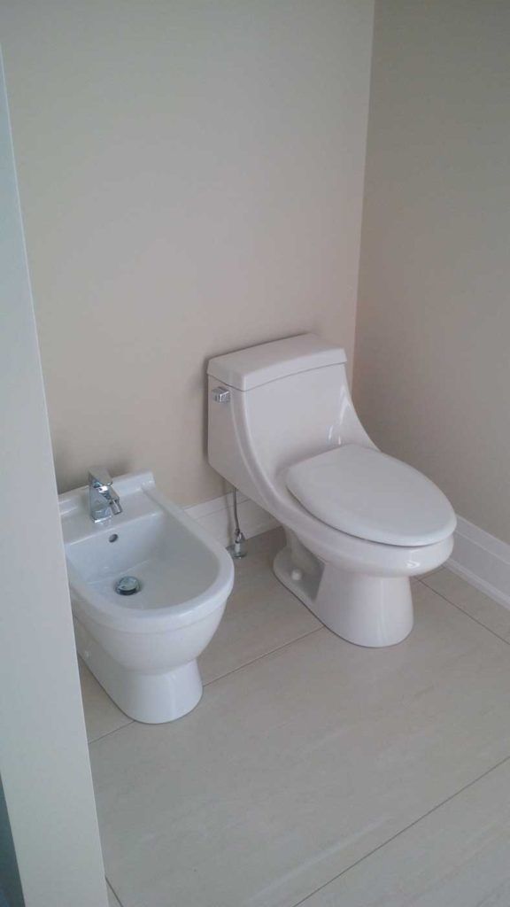 White bidet to the left of a white toilet in a white bathroom